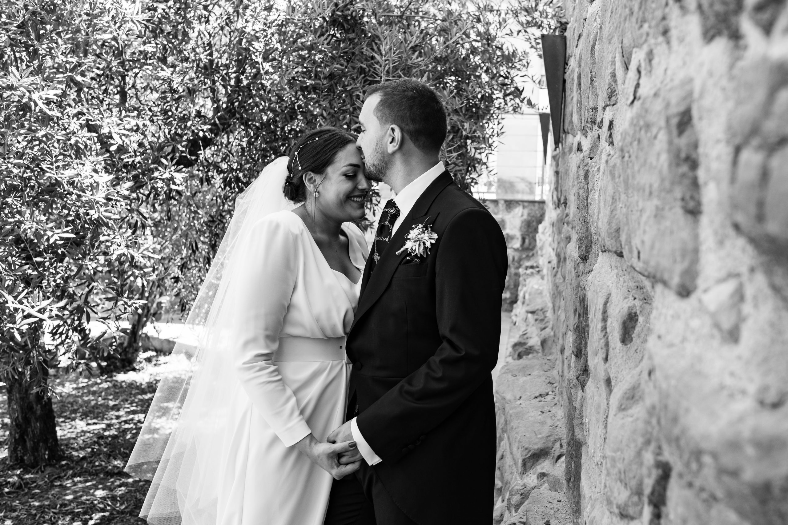 Foto en blanco y negro del novio besando la frente de la novia en un jardín
