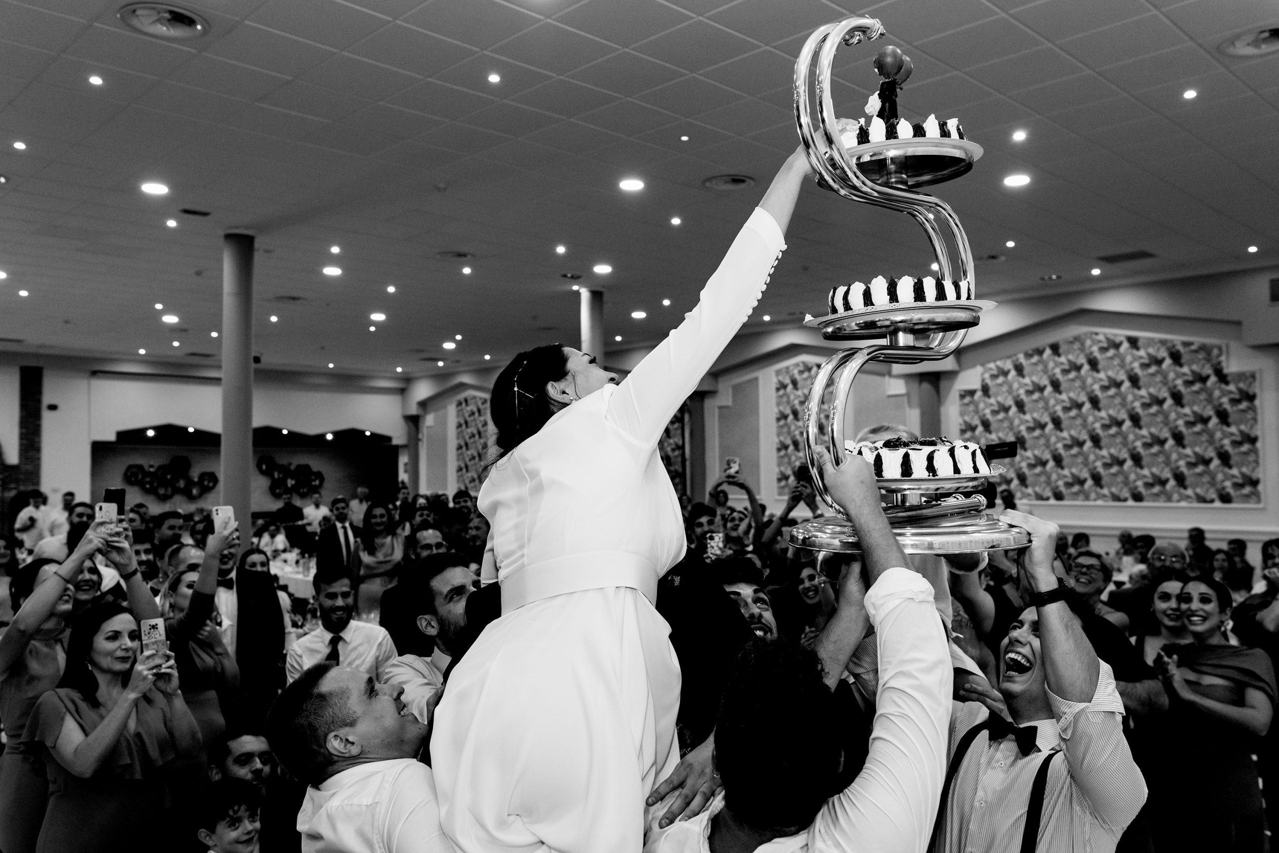Foto en blanco y negro de los familiares elevando la tarta y a la novia