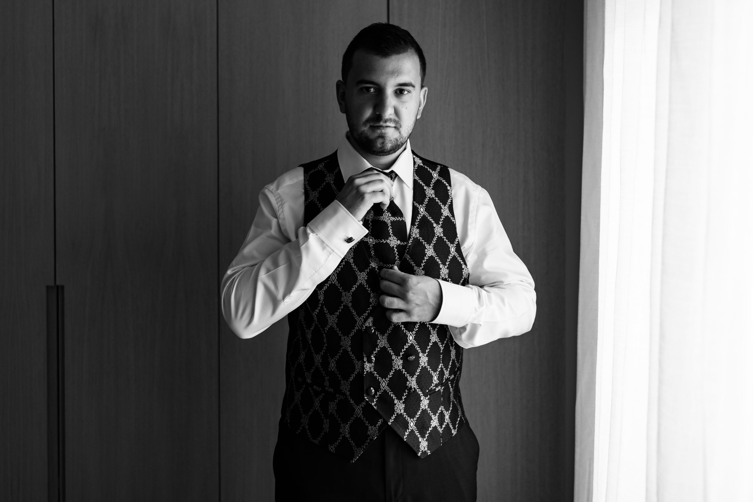 Foto en blanco y negro mirando a cámara colocándose la corbata a juego con el chaleco