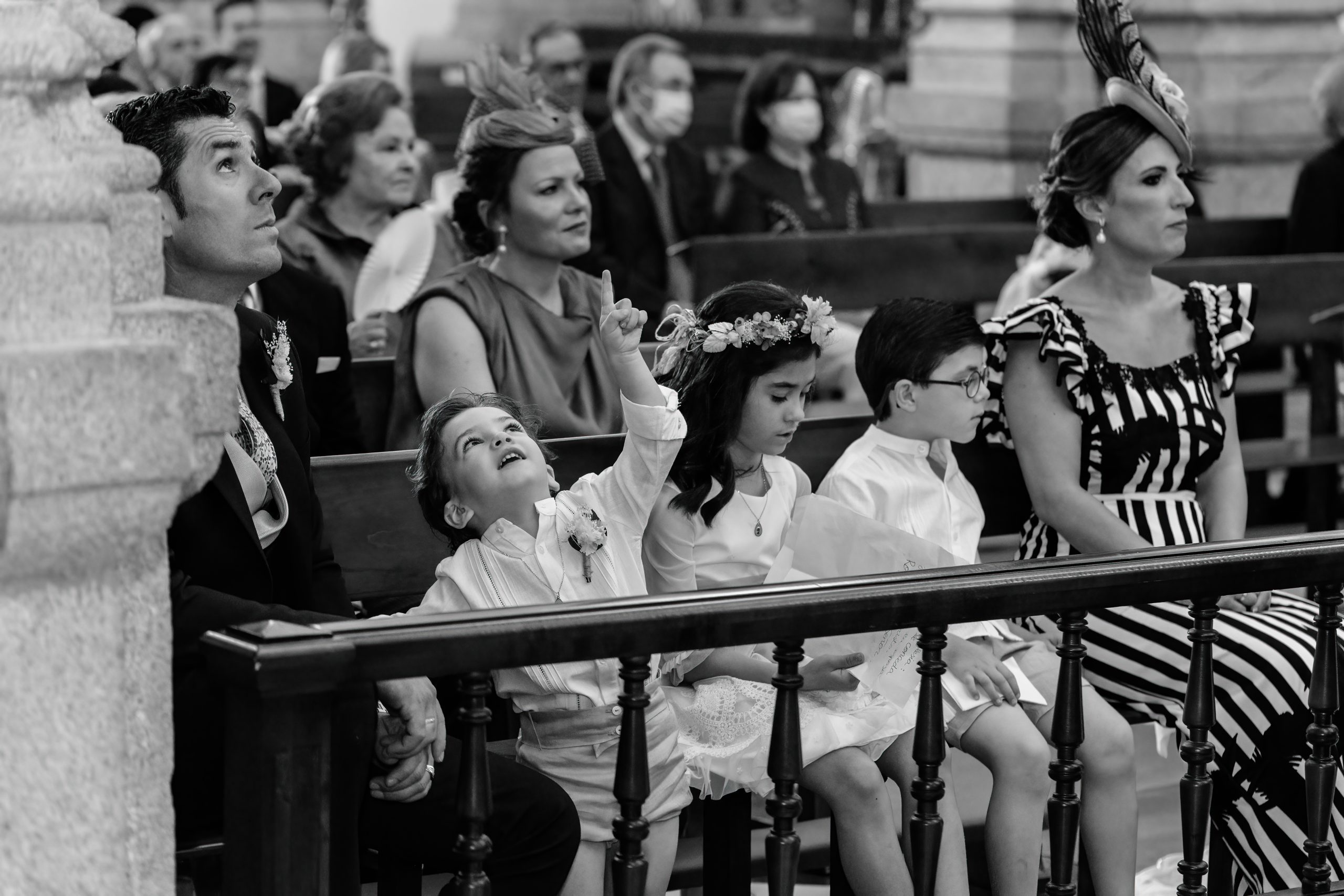 Foto en blanco y negro de los niños en la primera fila de los asientos de la iglesia mientras uno observa el techo curioso