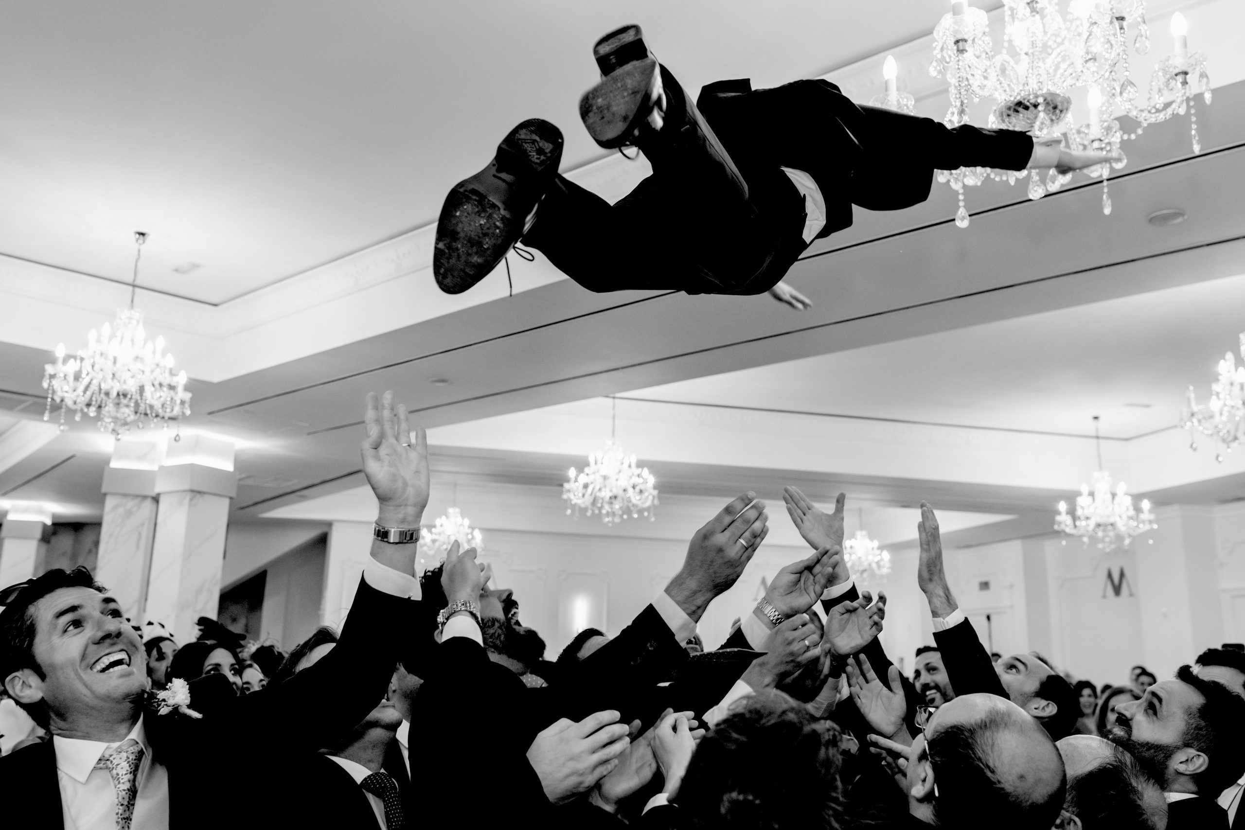 Foto en blanco y negro de los invitados levantando en el aire al novio
