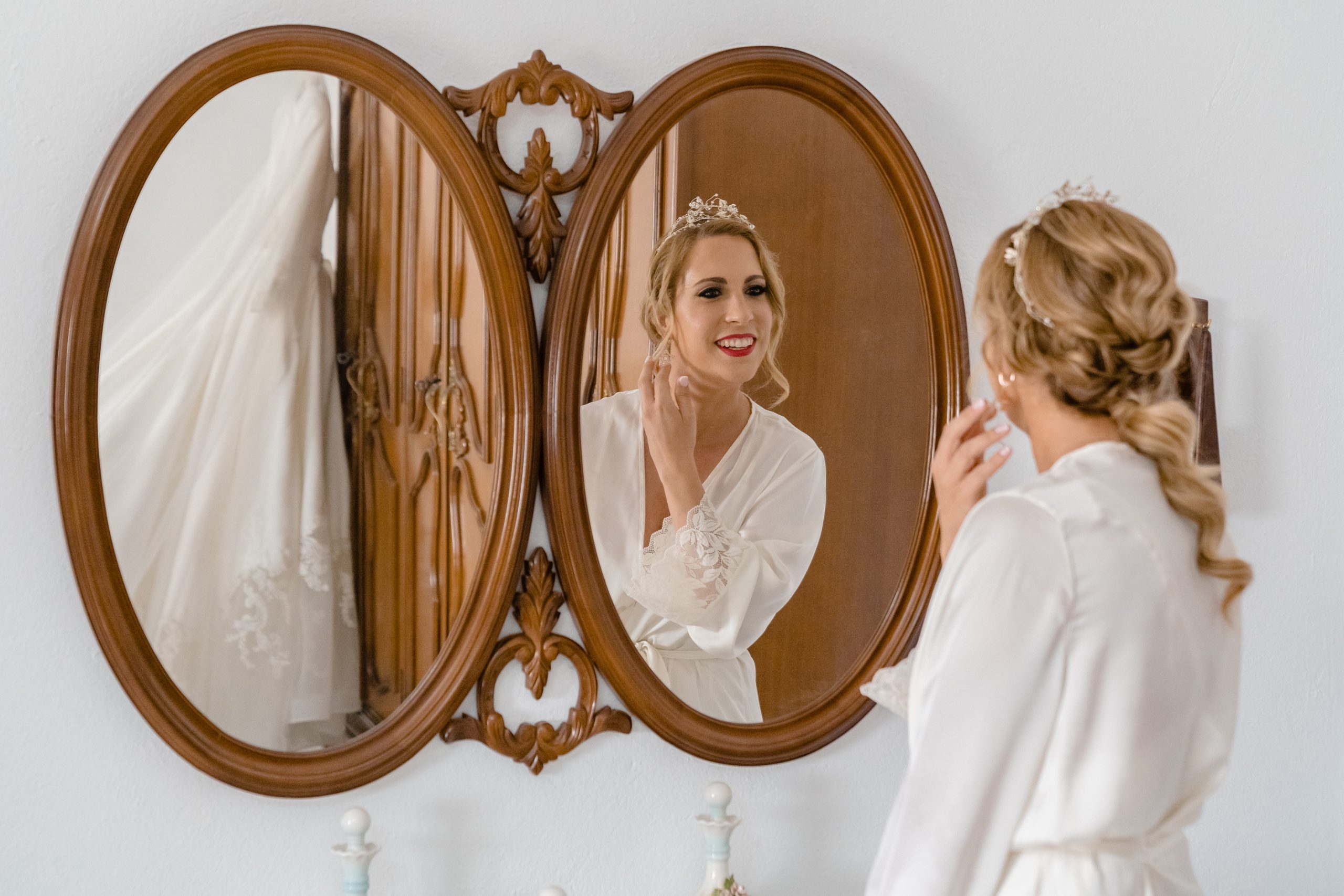 Novia mirándose por el espejo antes de ponerse el vestido, con una tiara en la cabeza y maquillada