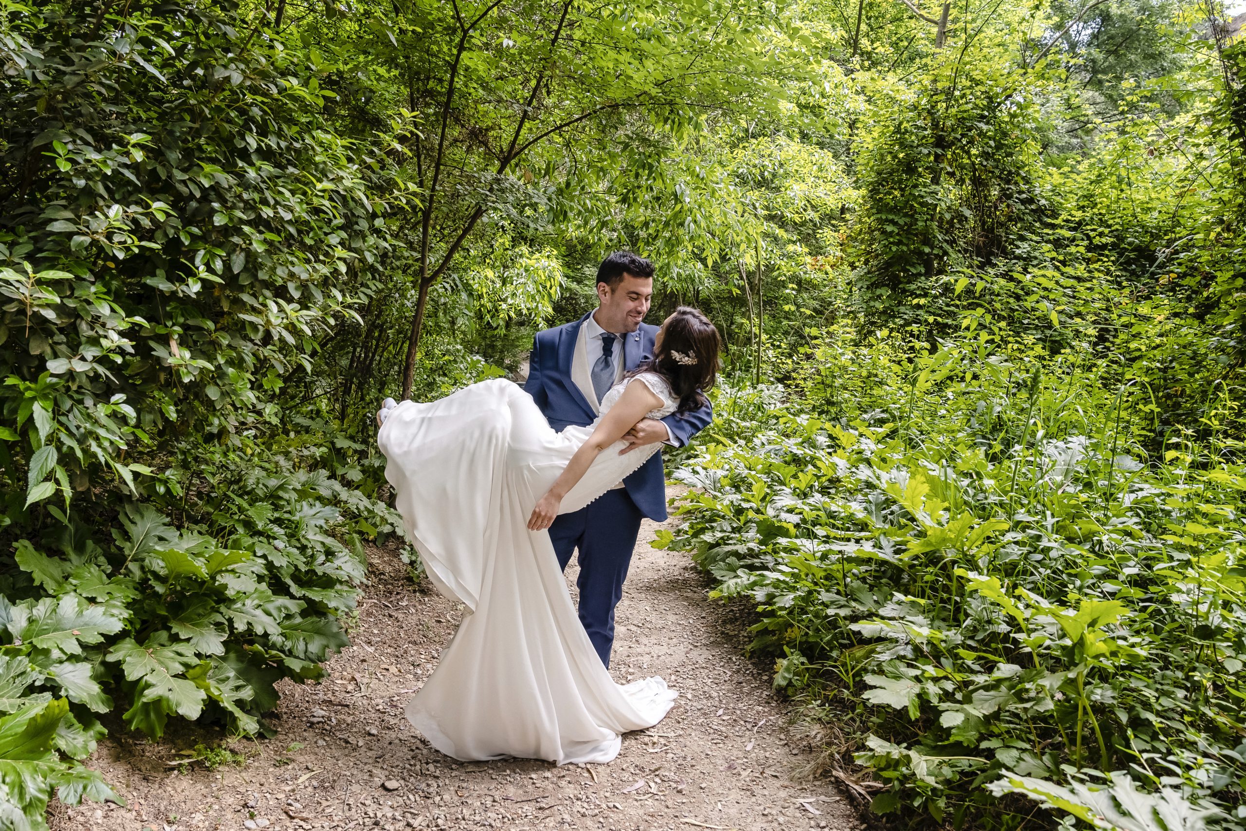 Novio sujeta en el aire a la novia en un sendero de un bosque