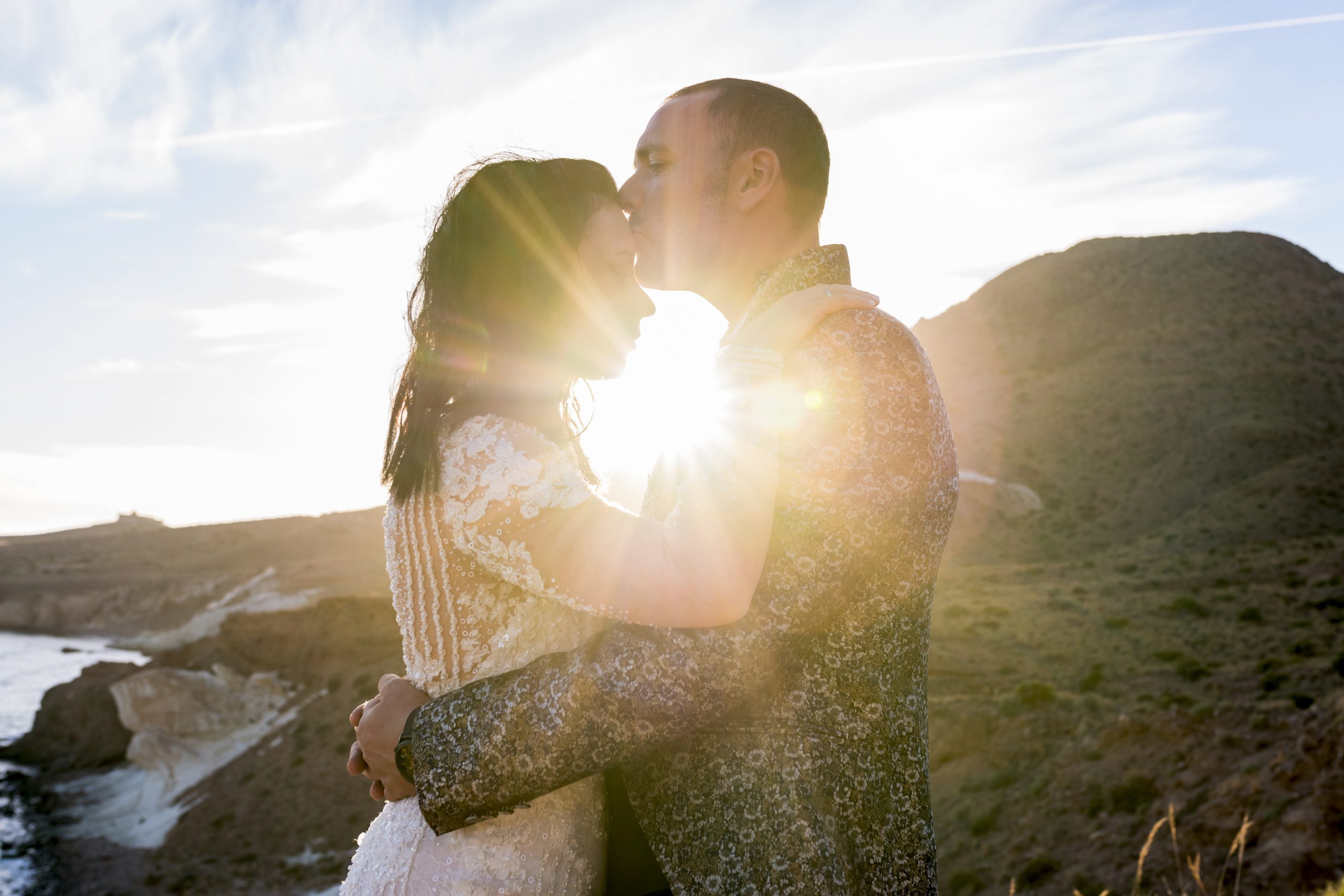 Novio besando la frente de la novia a contraluz de la puesta de sol