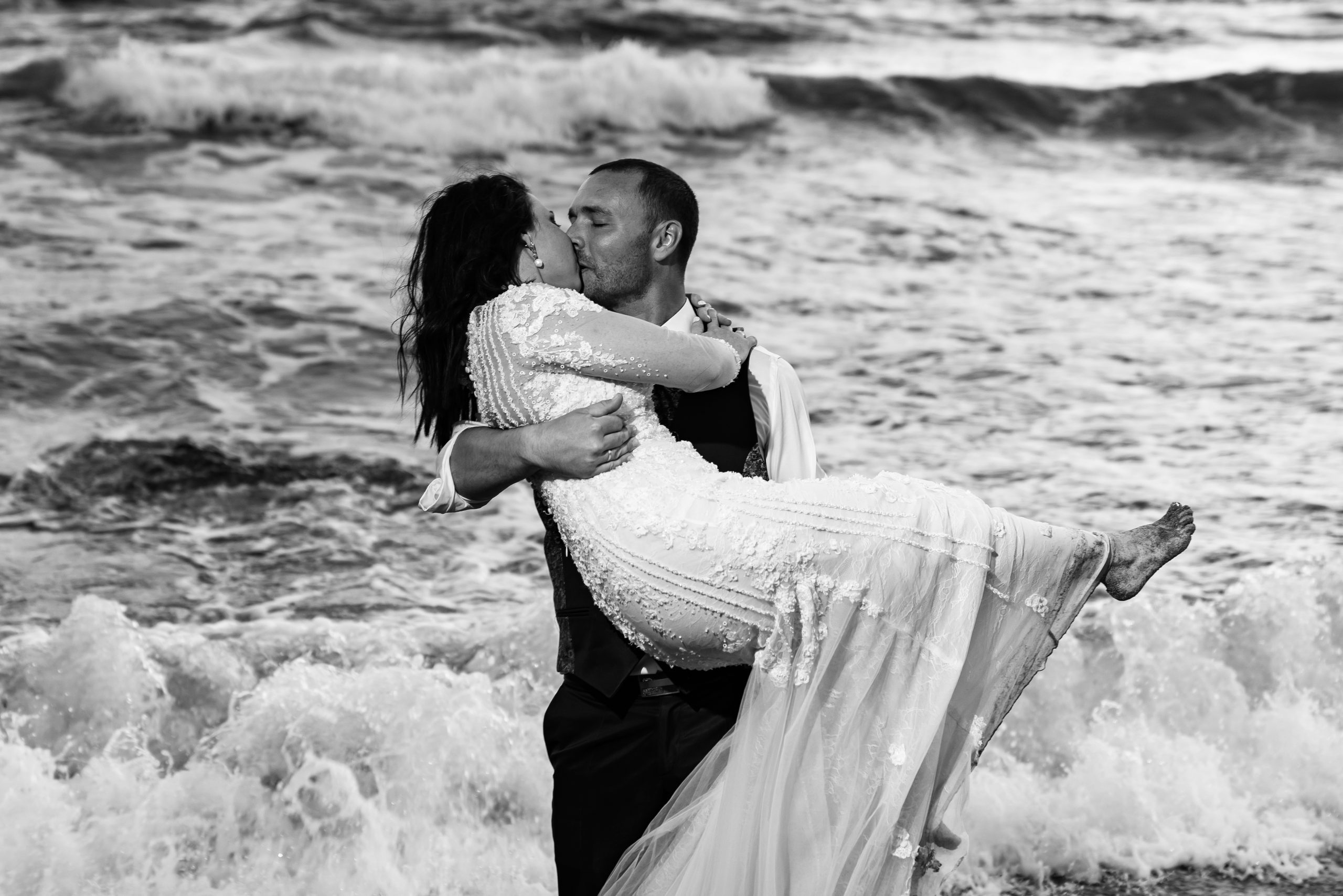 Foto en blanco y negro de los novios besándose en la orilla del mar