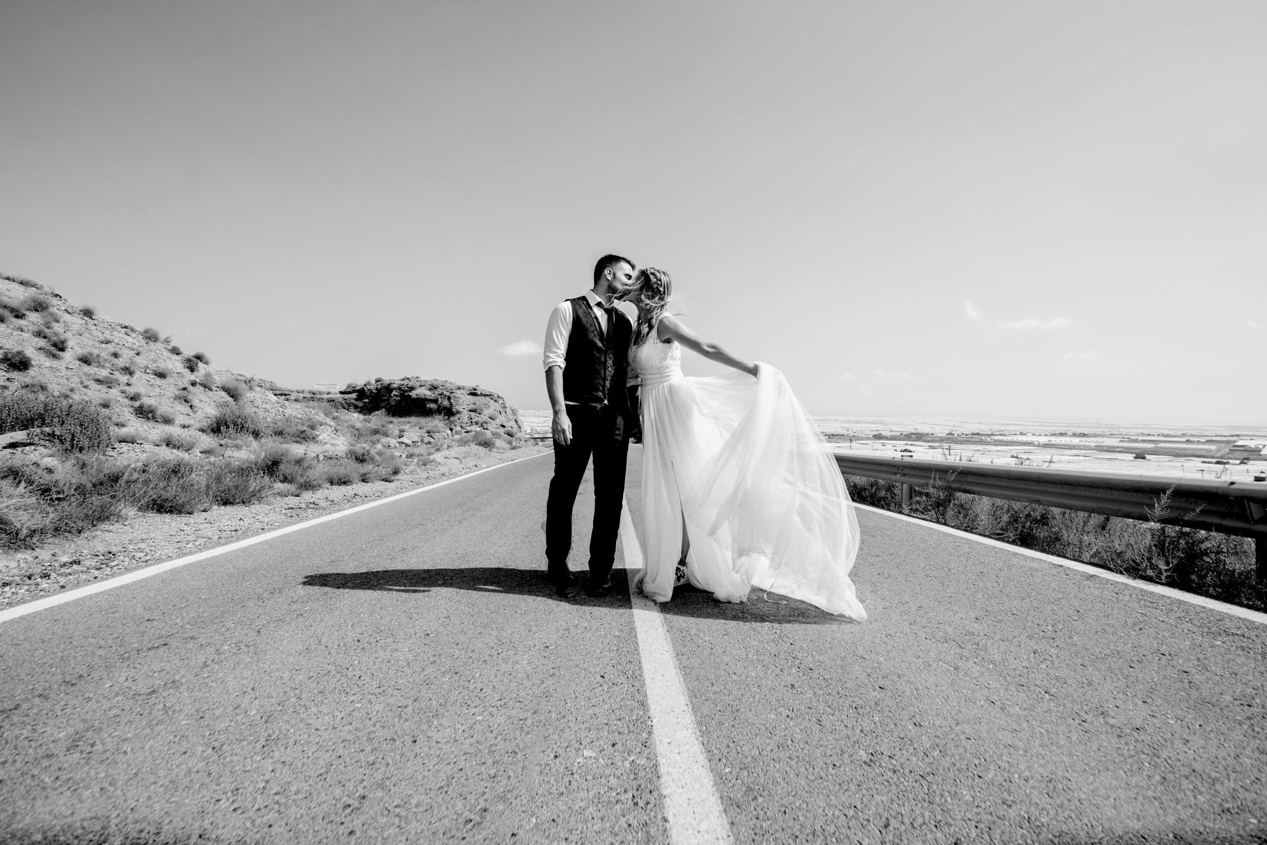 Foto en blanco y negro de los novios besándose en una carretera
