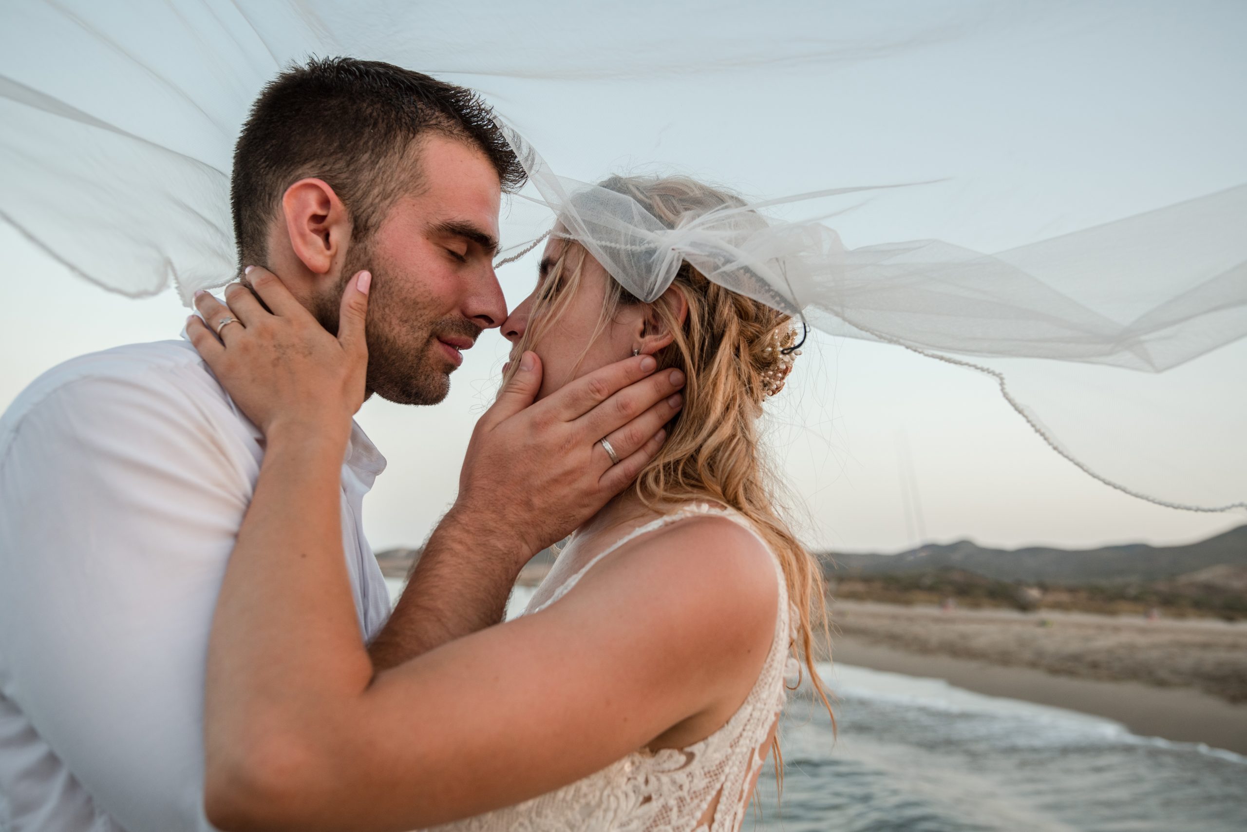 Novios a punto de besarse en el agua mientras el velo de la novia es movido por el aire