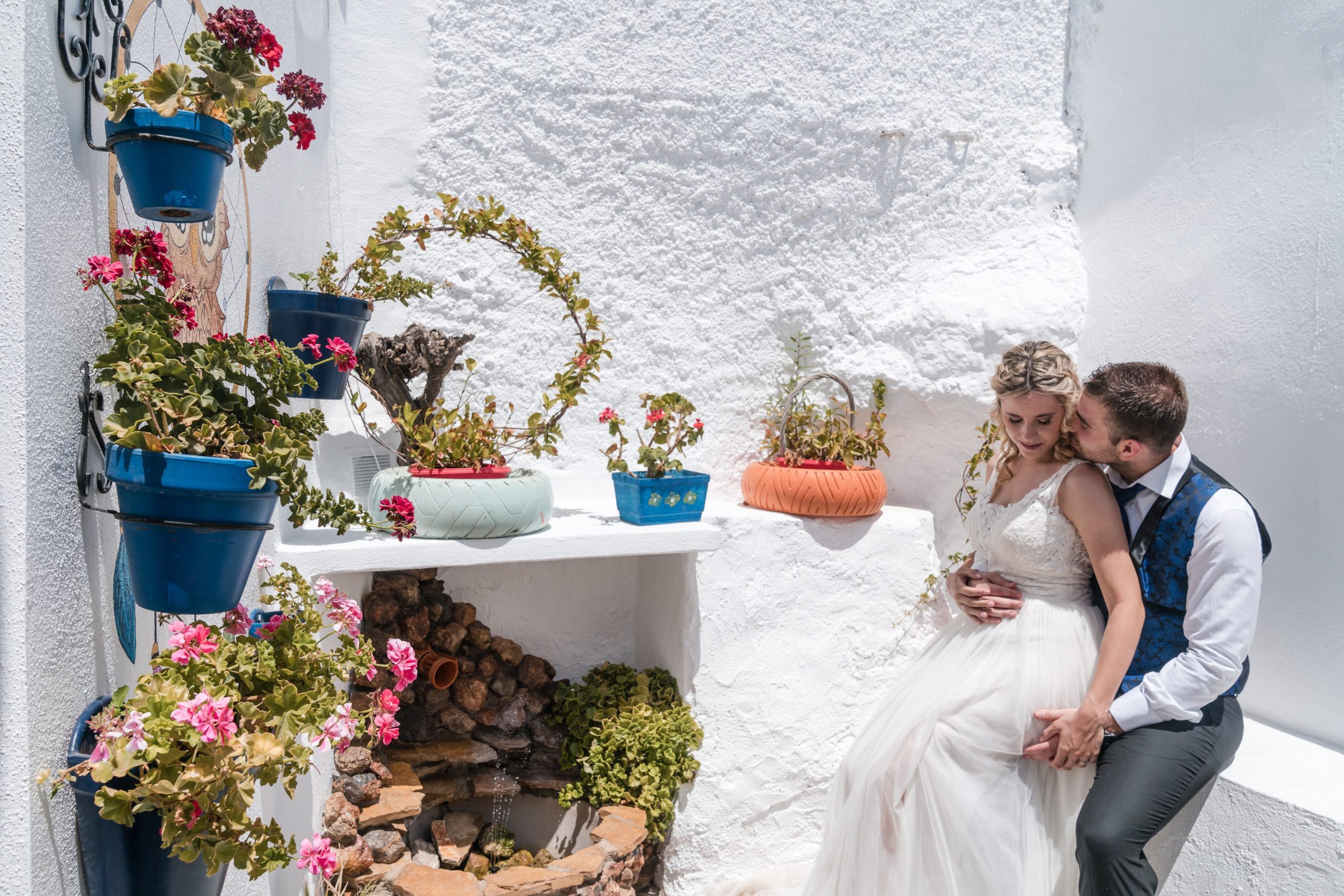 Novio esta sentado en un muro con la novia sentada en sus piernas al lado de una fuente