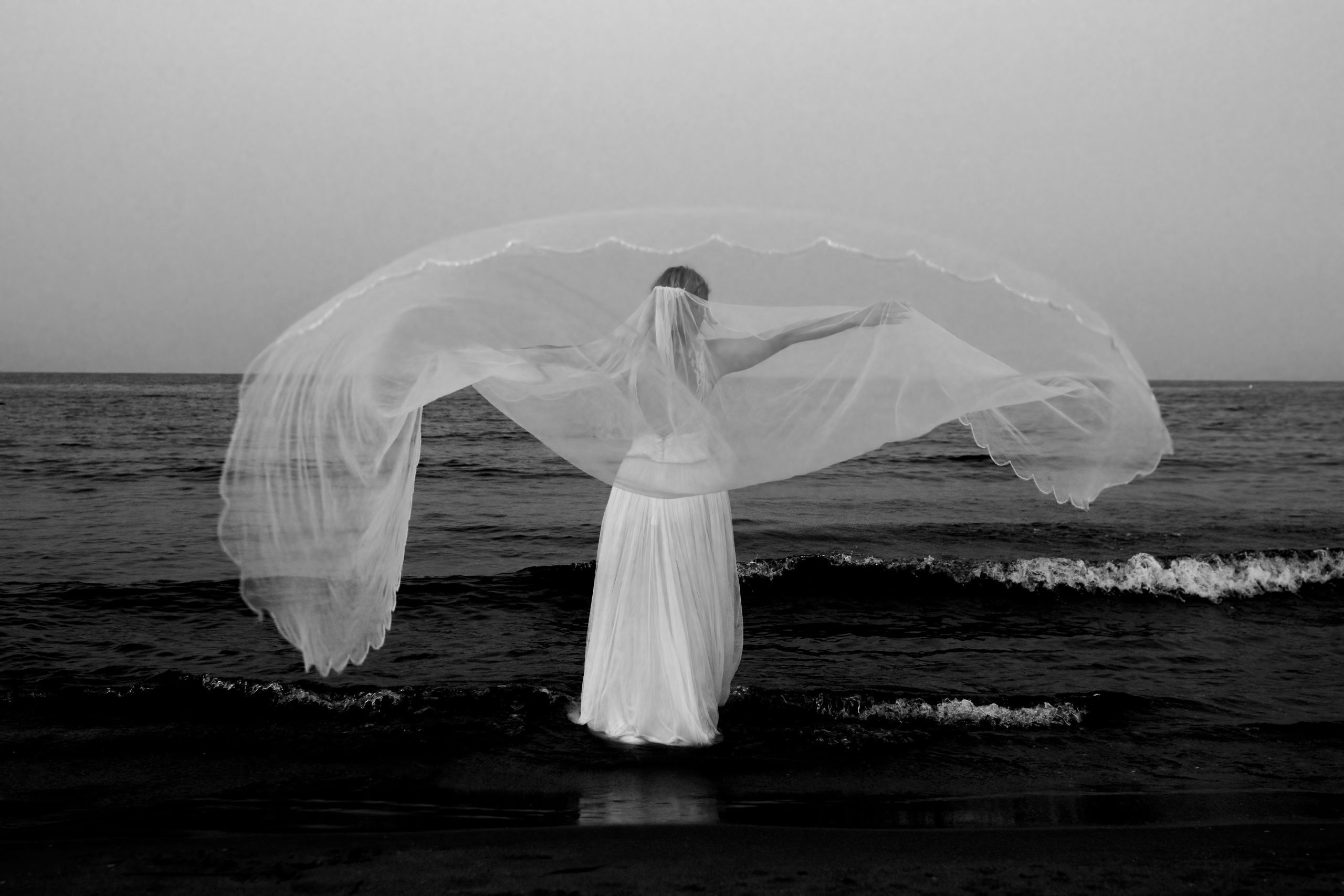 Foto en blanco y negro de la novia en la orilla ondeando su velo al viento